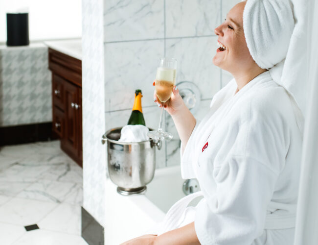 woman sitting on edge of bathtub drinking a glass champagne