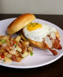 Breakfast sandwich with egg and bacon, served with seasoned potatoes on a plate.
