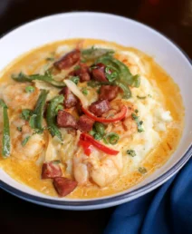 A comforting bowl of shrimp and grits topped with sausage, peppers, and herbs.