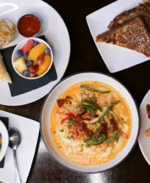 A delicious brunch spread with fruit bowl, pancakes, wrap, and eggs in a cosy setting.