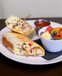 Savoury breakfast burrito and fresh fruit bowl on a white plate.