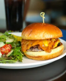 Gourmet burger and fresh salad served on a plate in a cosy restaurant setting.