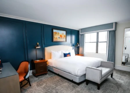 Elegant hotel room with king bed, blue accent wall, and cosy seating area.