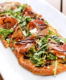 Gourmet flatbread with prosciutto, rocket, and balsamic glaze.