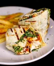 Grilled chicken wrap with chips on a white plate, garnished with fresh herbs.