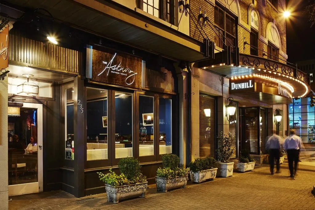 The exterior of a hotel at night with a sign reading 'Dunhill' and planters in front.