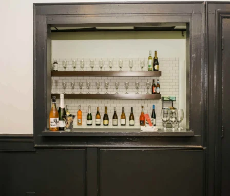 Cosy hotel bar with wine bottles and glasses on shelves.