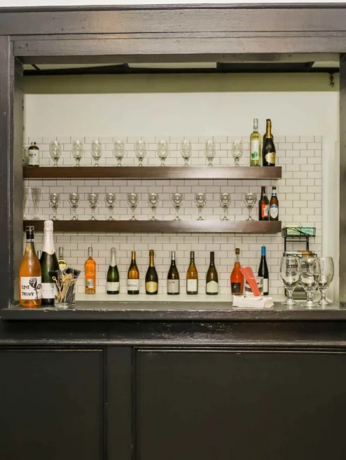 Cosy hotel bar with wine bottles and glasses on shelves.