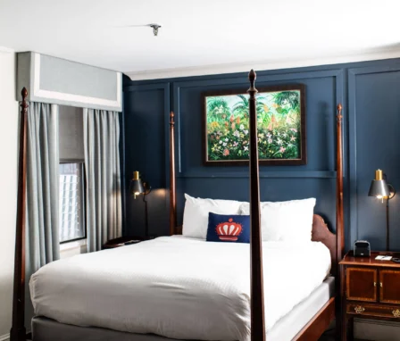 A hotel room with a four-poster bed, dark wood furniture, and a blue accent wall featuring artwork.